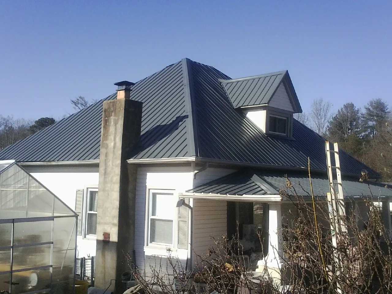 Dark blue standing seam metal roof on a white farmhouse with dormer — Slate & Tile Roof Repair by Roofing Brothers in Albemarle
