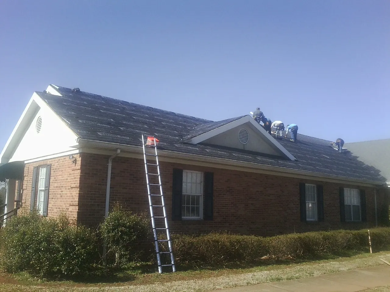 Crew tearing shingles off a brick ranch roof with a ladder set — Metal Roof Repair work by our crew in Albemarle