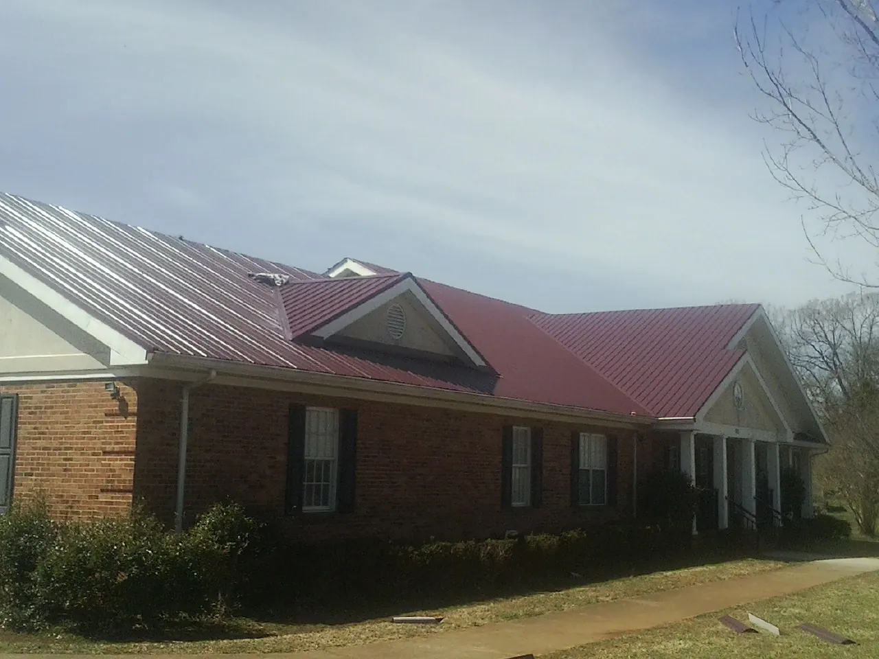 Red metal roof with gabled entries on a long brick building, from a Hail Damage Roof Repair job in Albemarle