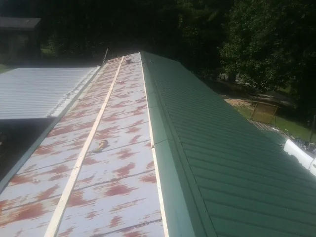 Old rusted panels beside newly installed green metal roofing — Wind Damage Roof Repair by Roofing Brothers in Albemarle