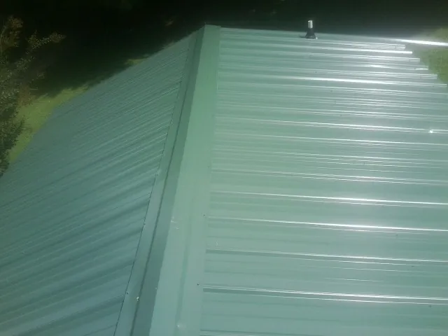 New green metal panels meeting at the ridge of a roof — Flat Roof Repair work by our crew in Albemarle