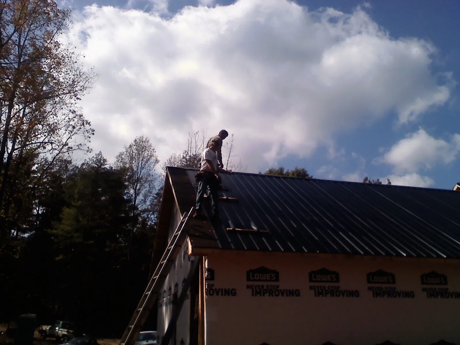 Roofer fastening dark metal panels high against a cloudy sky, from a Roof Inspection job in Albemarle