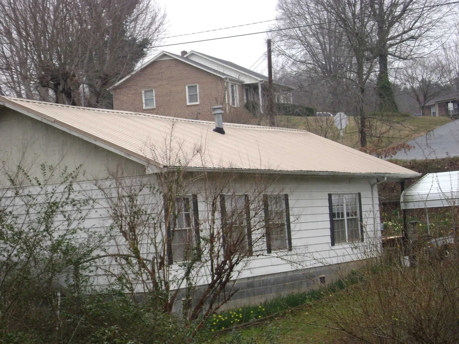 Tan metal roof on a white sided house set into a hillside — Commercial Roofing by Roofing Brothers in Albemarle